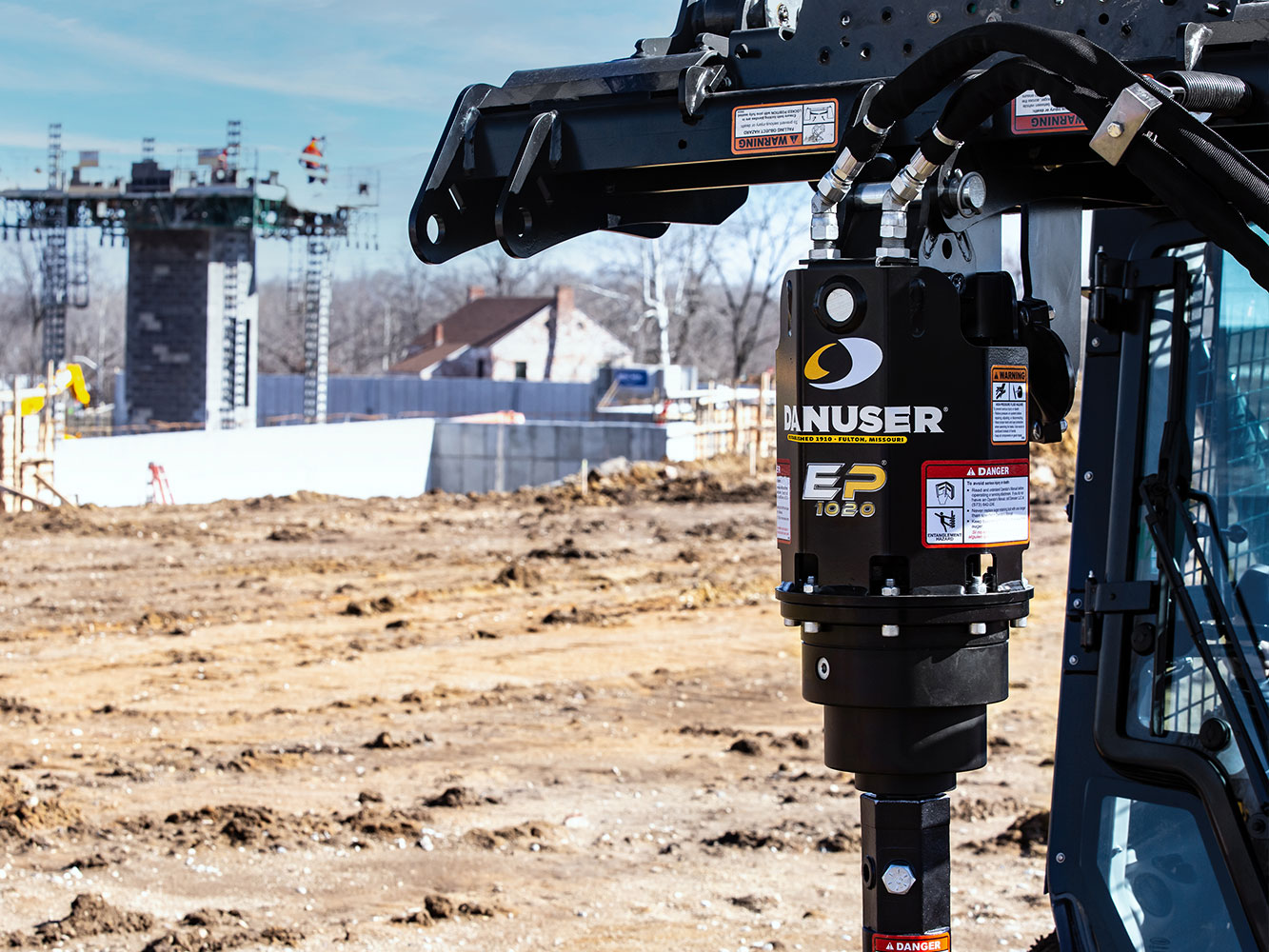 Image showing close-up of Danuser EP 1020 Auger Drive on skid steer at construction site with equipment and unfinished building