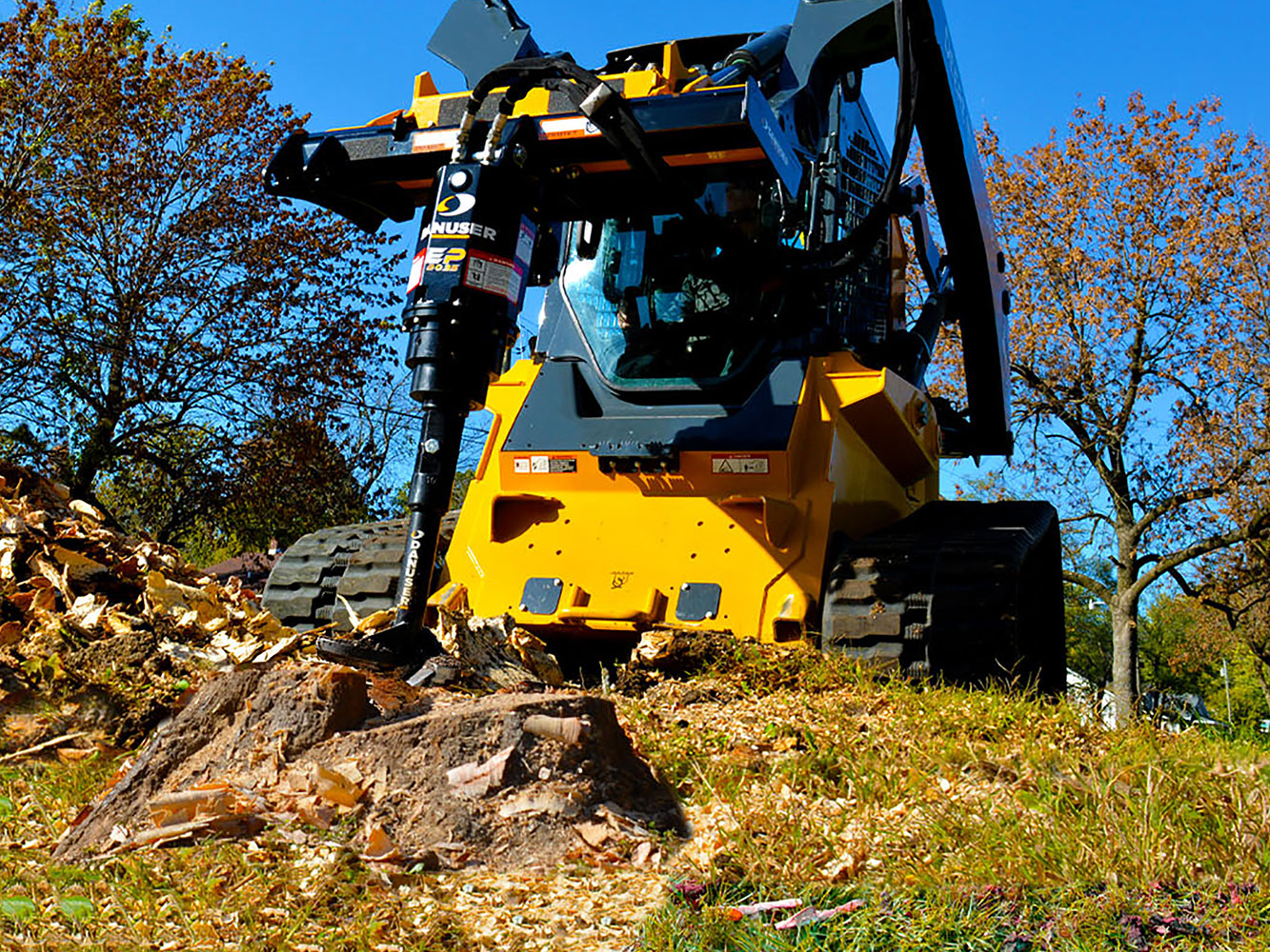 Image showing Danuser EP 2035 Auger Drive on John Deere 333G Skid Steer drilling into tree stump a top grassy hill