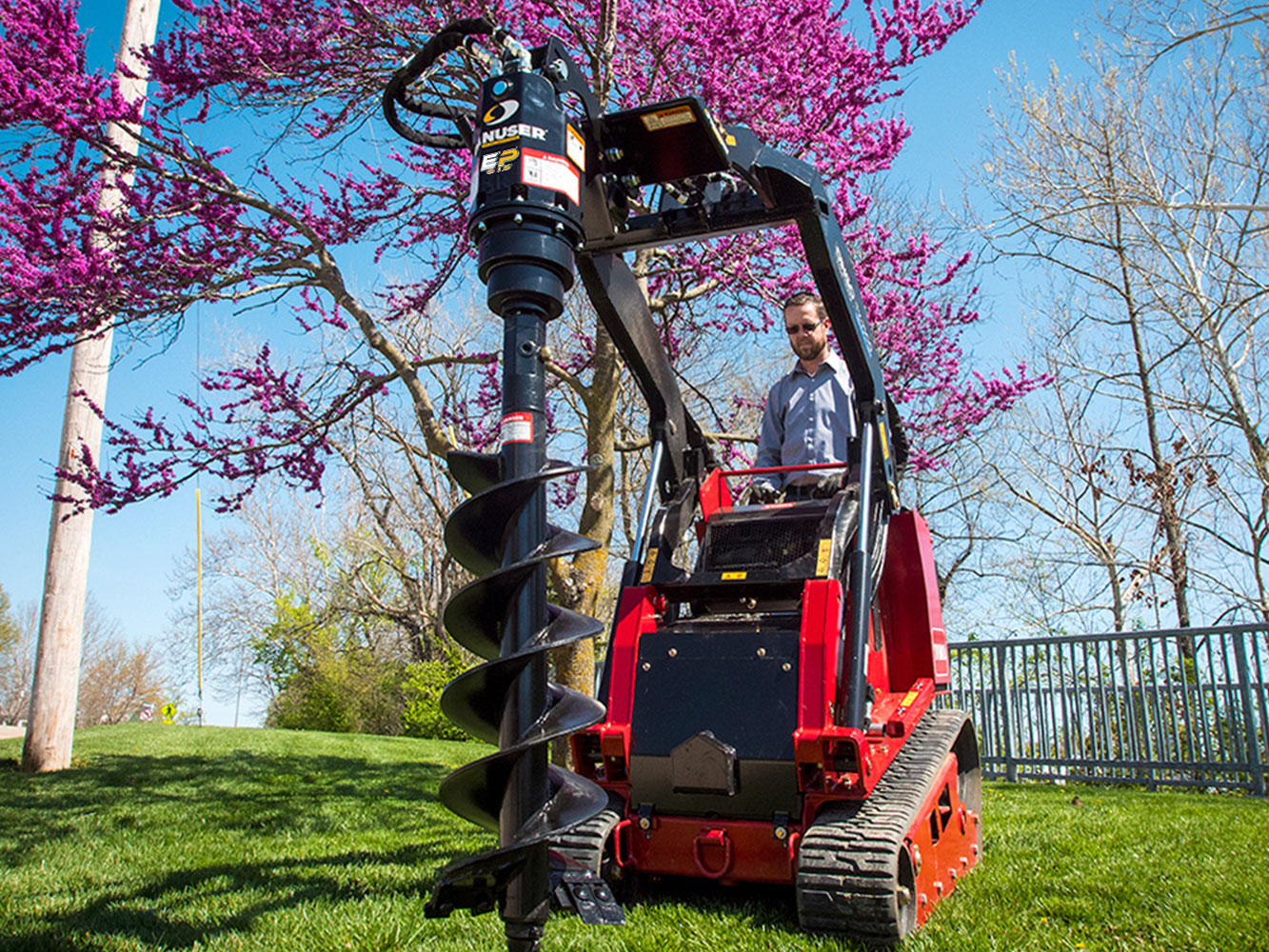 Image showing Danuser EP 615 Auger Drive on Toro Mini Skid Steer in grassy area and pink tree visible in background