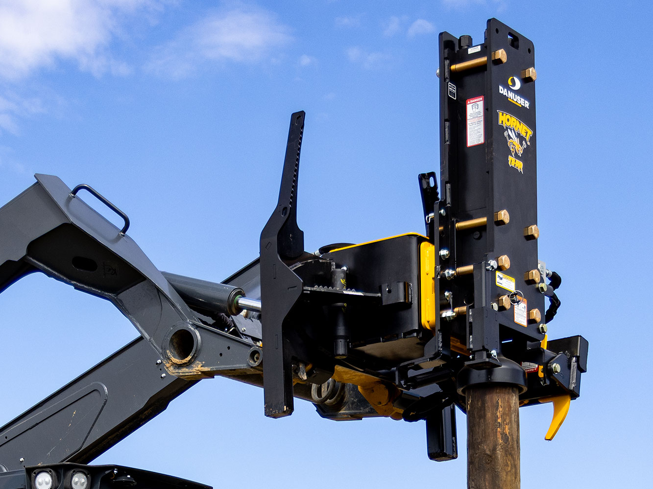 Image showing Danuser Hornet T8-RR on John Deere 333G Skid Steer shown close-up with wooden post and clear blue sky in background