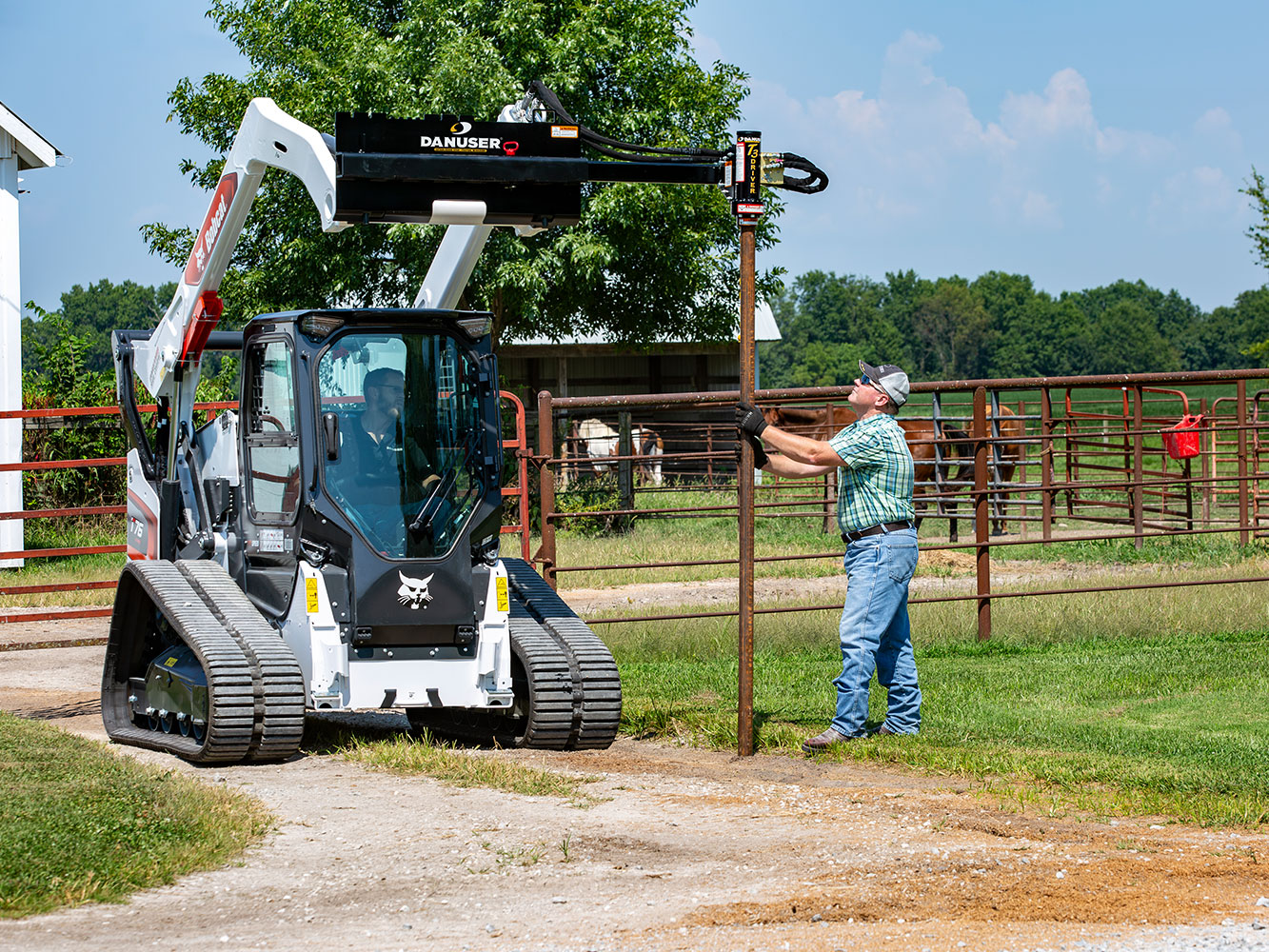 Image shows Danuser T3 on Bobcat T75 drives post into ground while man holds it; horses, fence, and buildings in background