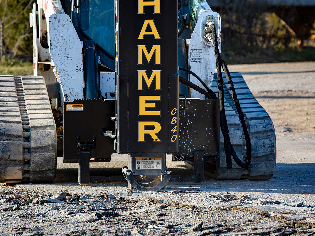 A skid steer loader equipped with a Hammer CB40 hydraulic breaker attachment is breaking up concrete or asphalt. 