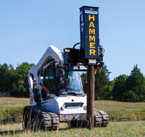 A skid steer hammer post driver in a field.