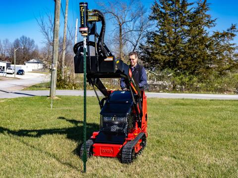 Image of Danuser T3 post driver on Toro DINGO TX427 Mini Skid Steer driving green post into ground on grassy area