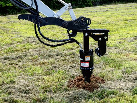 A Danuser EP2035 auger drive attached to a Takeuchi TB240 mini excavator, shown drilling into the ground in an open grassy field with trees in the background.