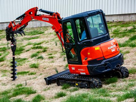 A Kubota KX033‑4 mini excavator equipped with a Danuser EP615 auger drive, positioned on a grassy slope with the auger bit extended toward the ground.