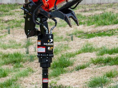 A close‑up view of the Danuser EP615 auger drive mounted on a Kubota KX033‑4 mini excavator, showing detailed features of the drive unit with the auger bit attached, positioned over a grassy area.