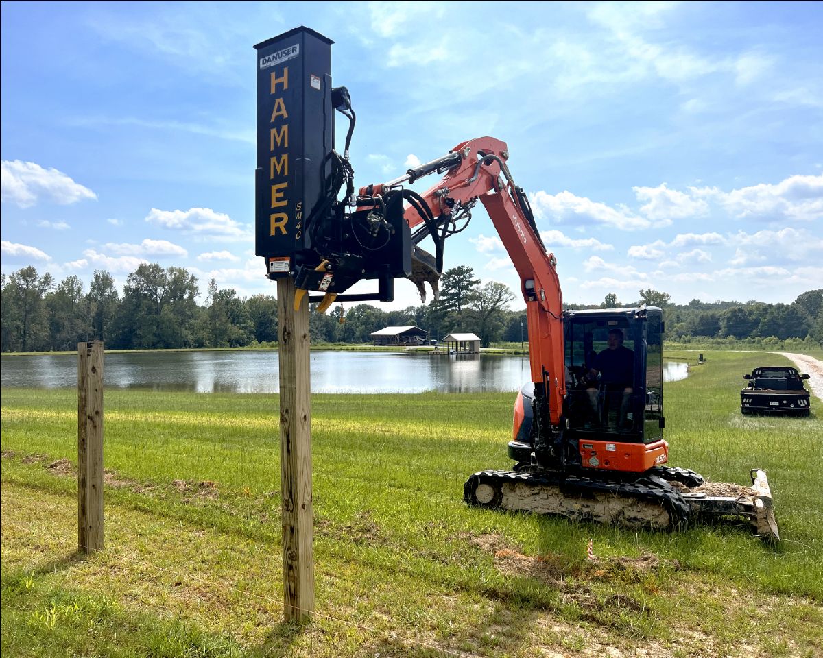 Hammer post driver on excavator pounding post into the ground